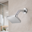 Set de ducha cuadrado cromado instalado en un baño moderno con cabezal, brazo y escudo visibles