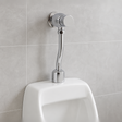 Fluxómetro temporizado instalado sobre un urinario en baño moderno