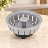Filtro plástico para canastilla de lavaplatos de 4 pulgadas suelto sobre piedra cálida antes de instalar; accesorios del ambiente no incluidos.