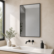 Espejo rectangular con marco metálico negro instalado en un baño moderno