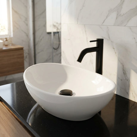 Close-up of oval-shaped black porcelain lavamanos with matte black faucet and push drain, emphasizing texture and reflections in natural light.